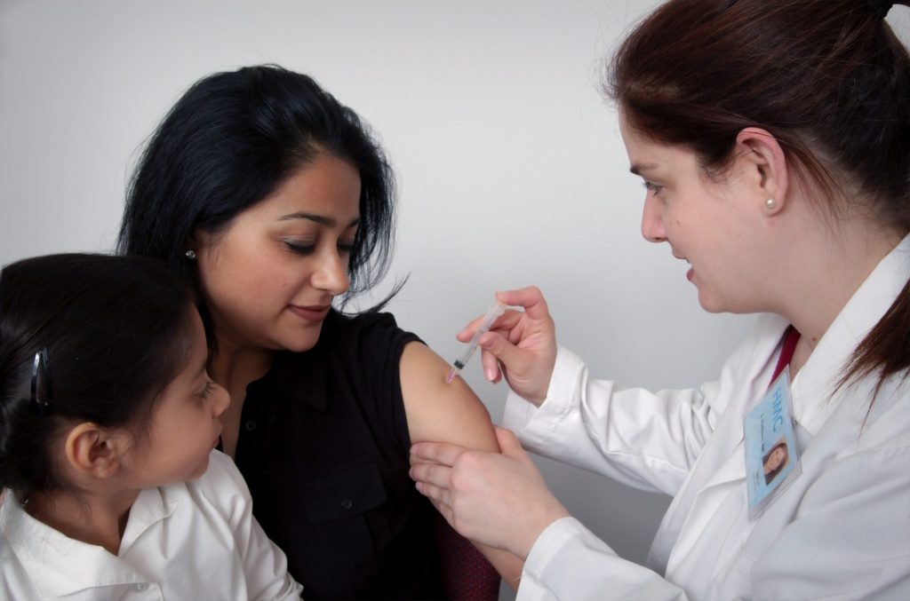 Healthcare provider administering vaccine to woman with child by her side.