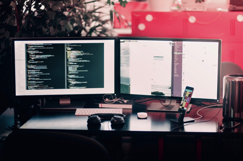 Website development coding desk image Two desktop monitors displaying website code and design tools on a modern workspace.