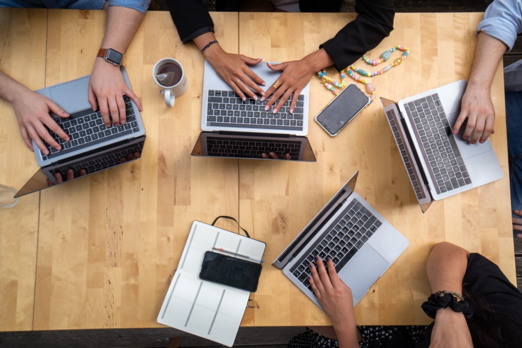 Team collaboration during a marketing strategy session. A group of people collaborating with laptops around a wooden table, working as a team.