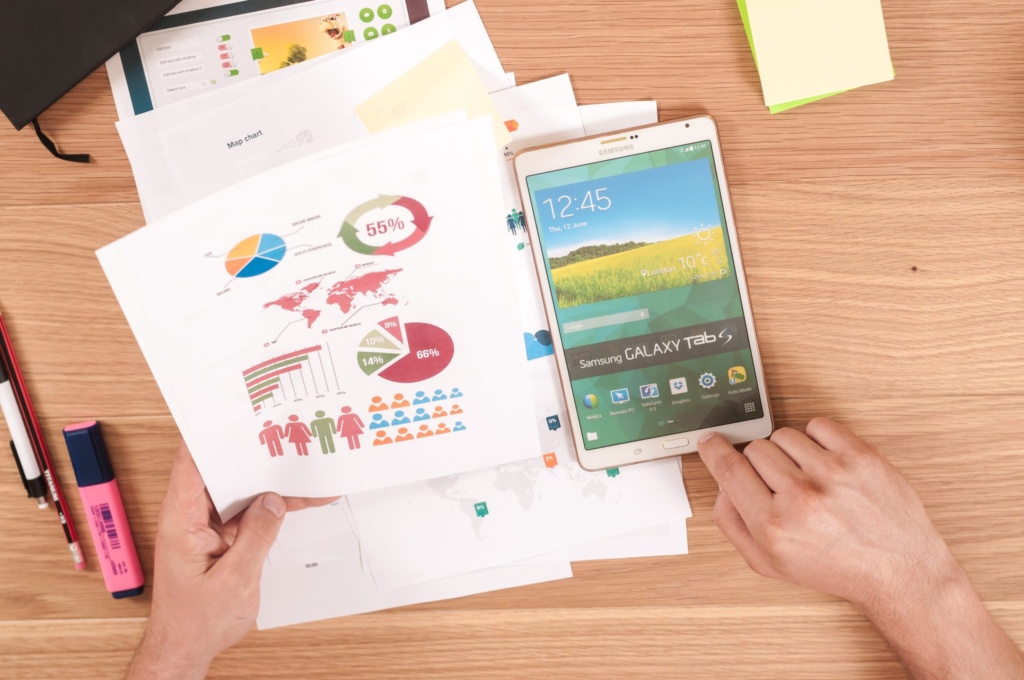 SEO data and analytics charts Person holding printed charts with infographics next to a Samsung tablet on a wooden desk