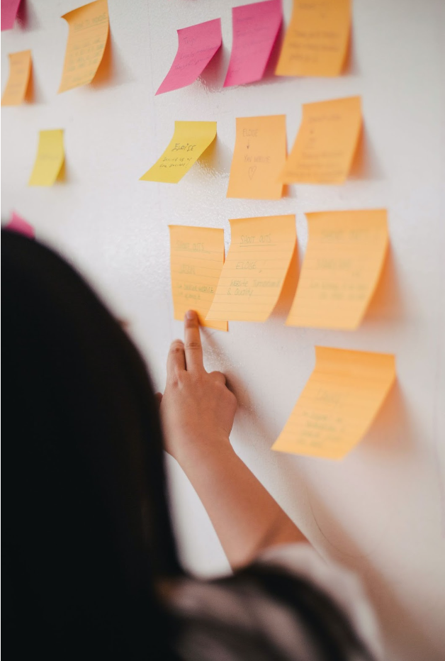 Brainstorming ideas with sticky notes on wall Person pointing to colorful sticky notes on a wall during a brainstorming session.