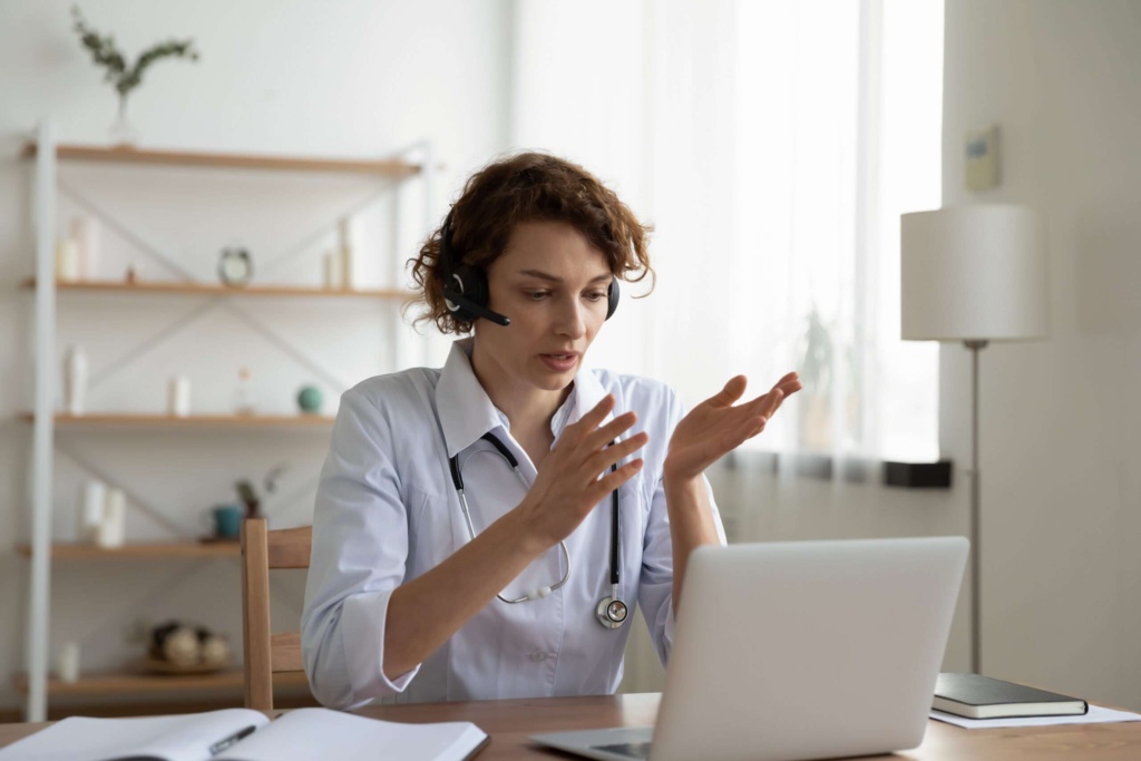 Doctor conducting telehealth video consultation Female doctor wearing a headset and white coat speaking during a telehealth video call on a laptop.
