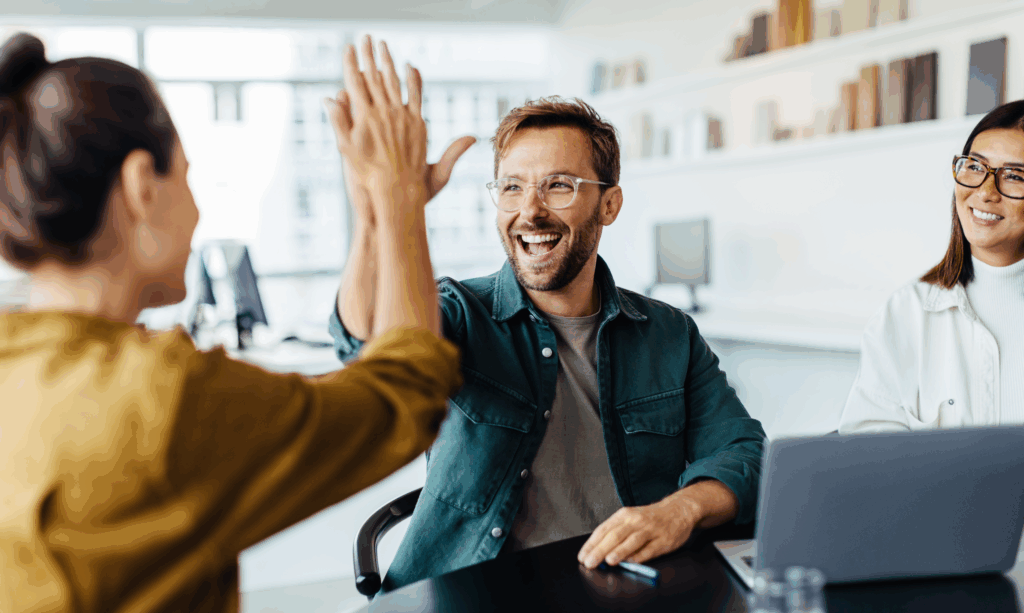 Team collaboration and success celebration in workplace setting Smiling coworkers in an office celebrating success with a high five during a collaborative meeting.