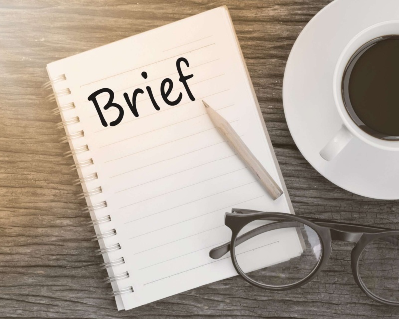 A notebook with the word "brief" written on it with coffee and glasses nearby