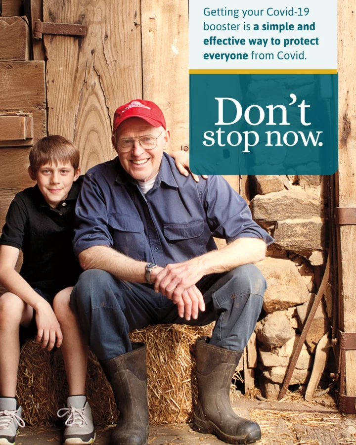 Man and grandson sitting together in a farm, encouraging people not to stop at just the COVID vaccine but getting the booster as well